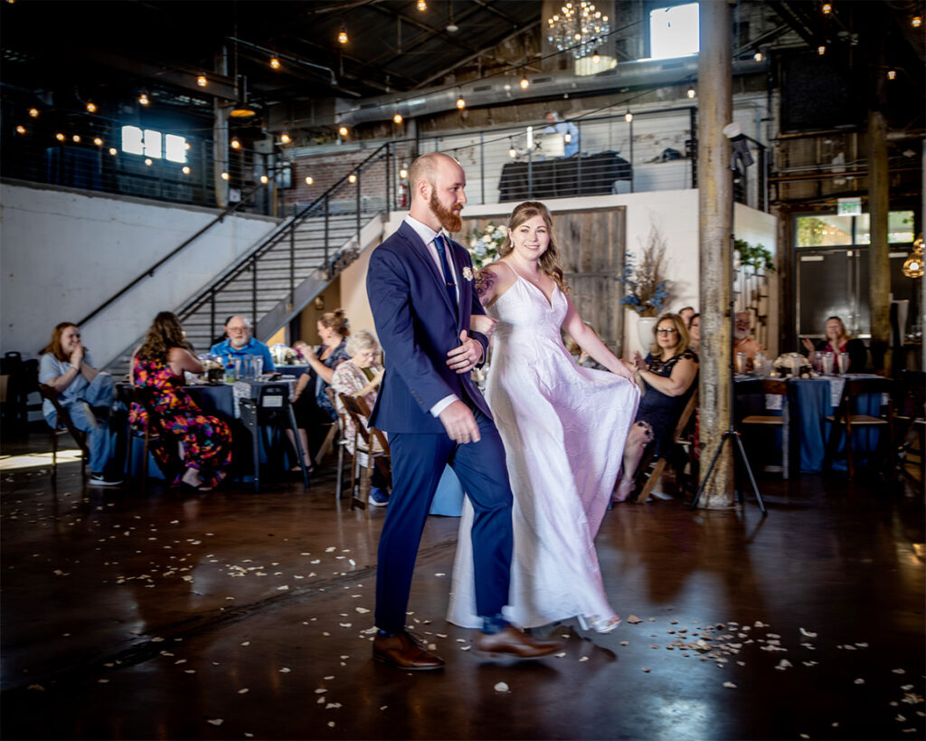 A bride and groom walking across a dance floor with guests behind them.