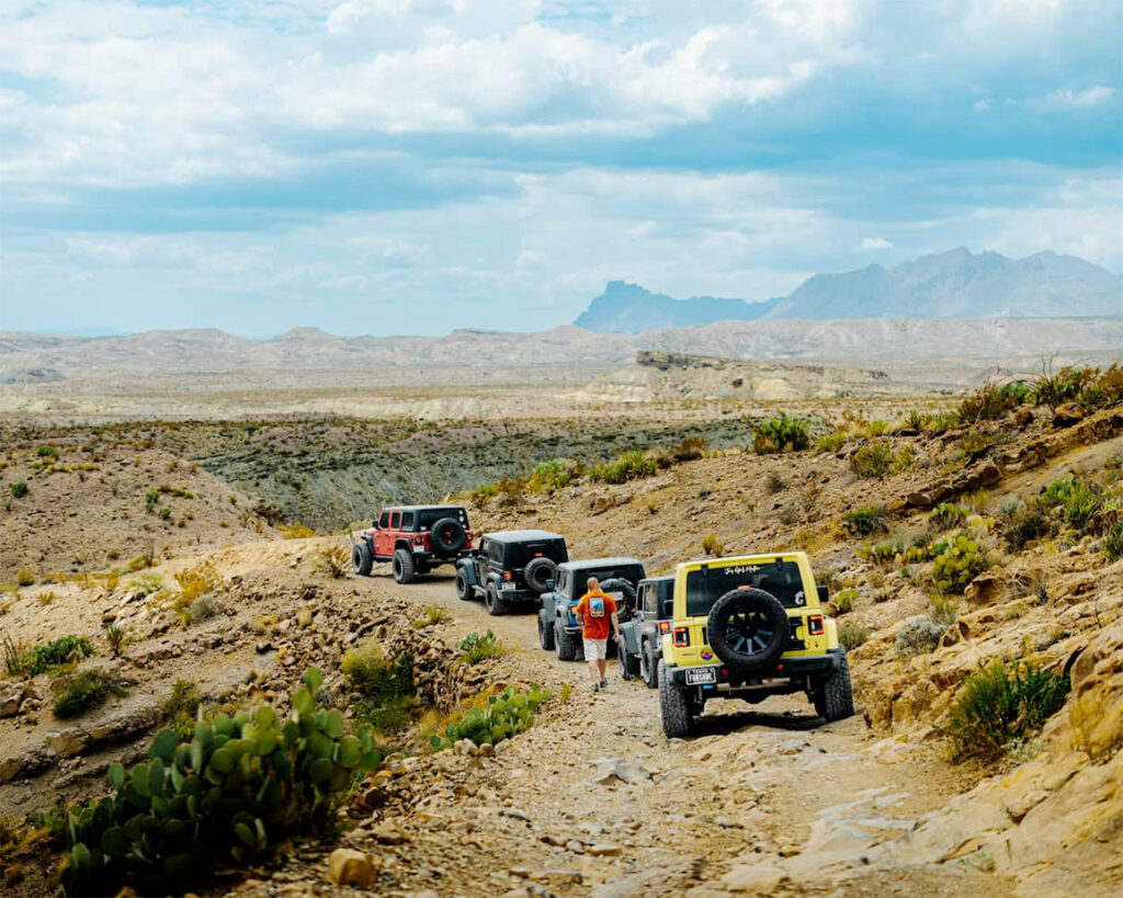 Five Jeep vehicles traveling along a rugged path towards mountains in the distance.