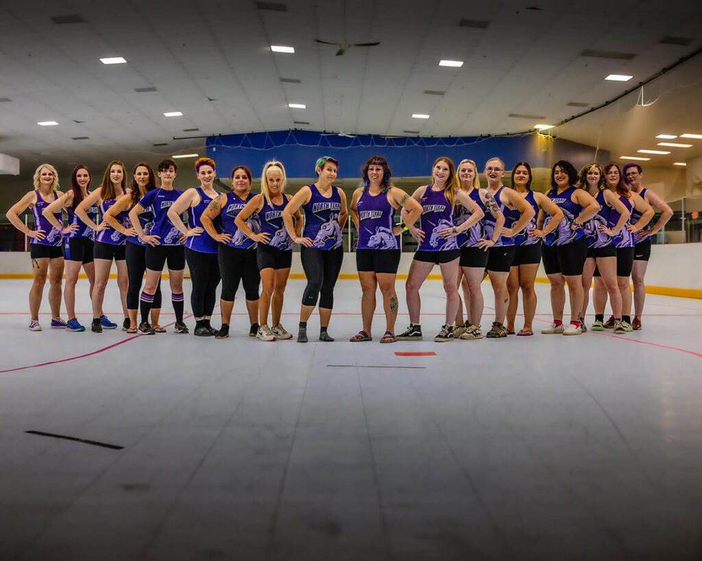 Members of the North Texas Roller Derby lined up on the floor of a skating rink.