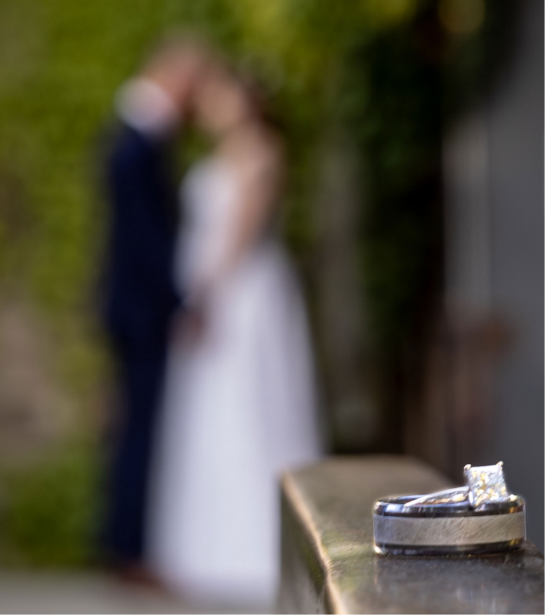 Wedding rings on a railing with a bride and grrom in the background
