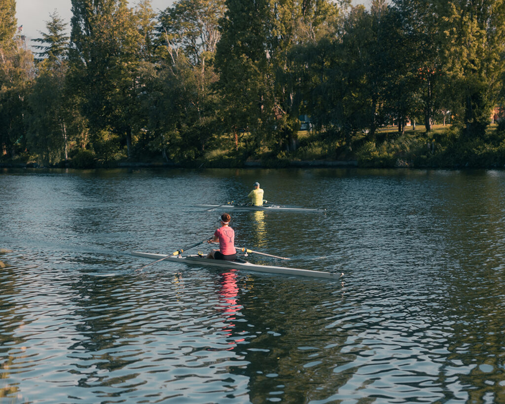 Two people in individual shells practicing rowing in a canal