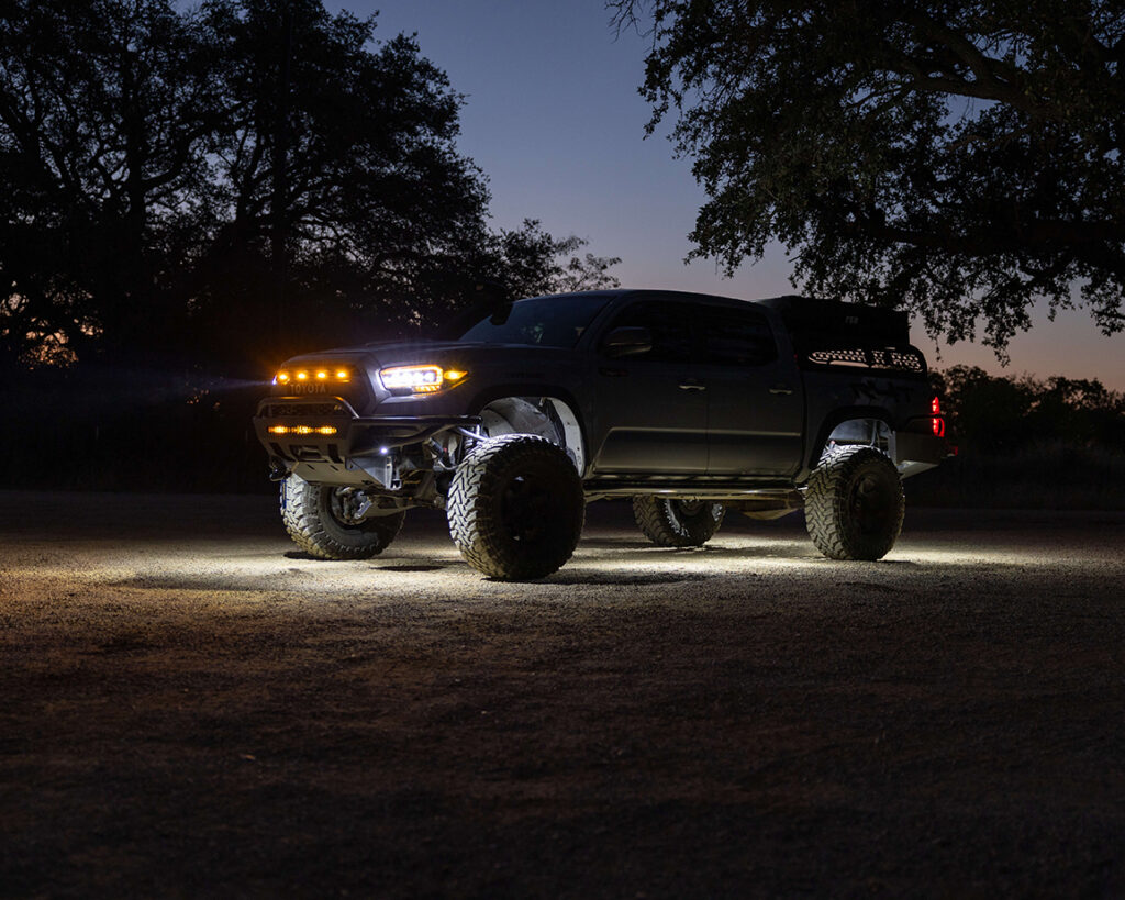 Toyota Tacoma early in the morning parked on dirt lot with headlights, running lights, and rock lights turned on