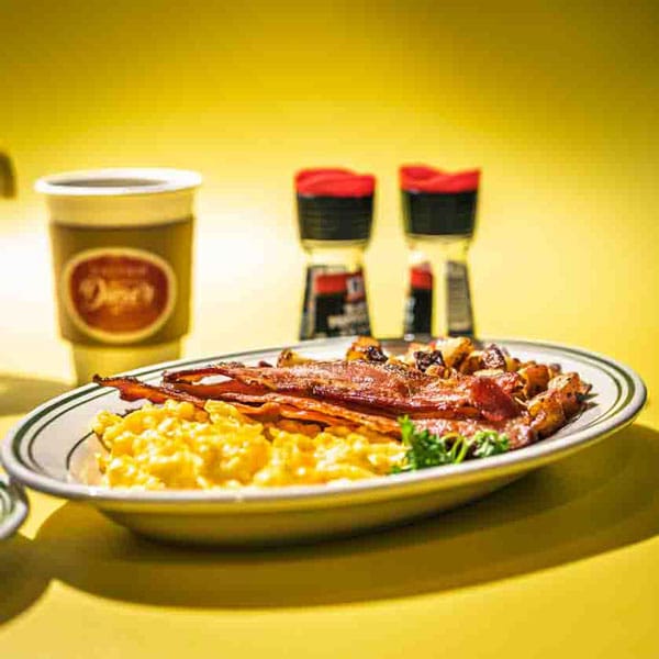 Daytrip-Diner-Social-Media-Images a plate with scrambled eggs, bacon and potatoes on a bright yellow background