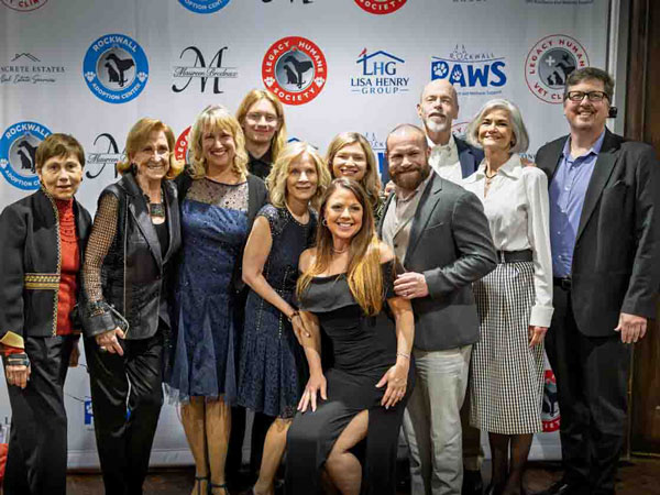 LegacyofLove-Gala-Group-Photo A row of 11 people standing in front of a step and repeat sign while smiling at the camera.