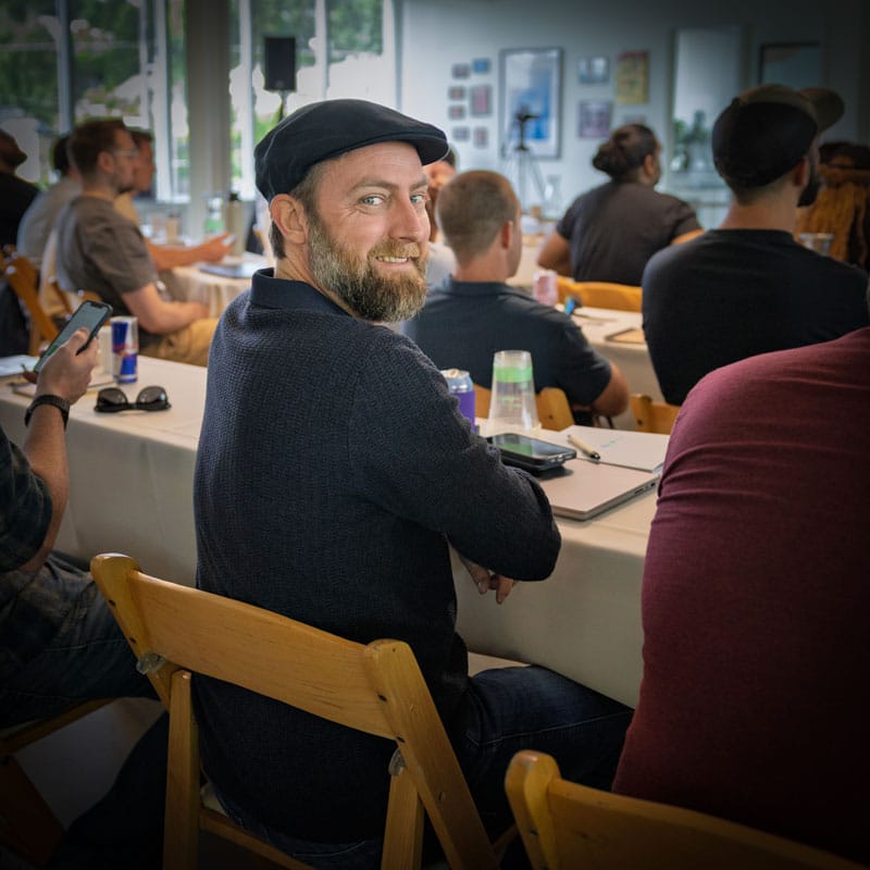 event-photography-seattle-rich-noah-creative a caucasian male seated at a table wearing a hat and looking over his right shoulder smiling at the camera.