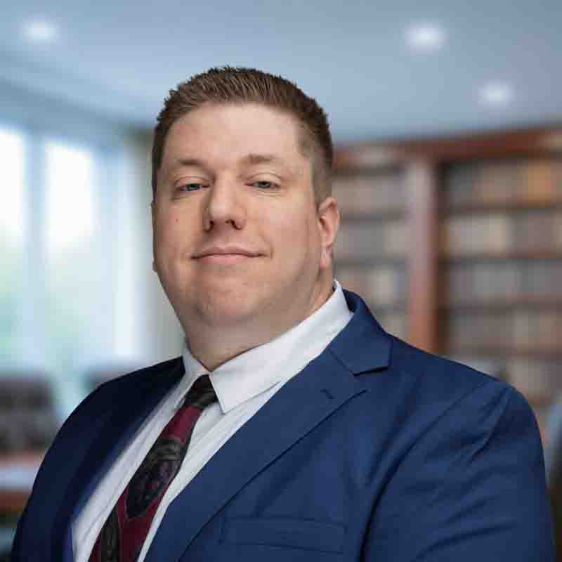 caucasian male wearing a blue suite, white shirt, and maroon tie.