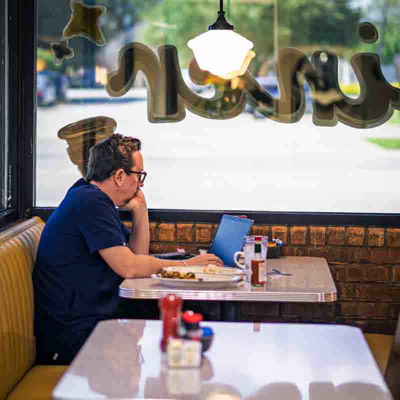 restaurant-customer-daytrip-diner-grapevine-texas a caucasian male restaurant customer seated at a table and looking at a laptop while eating breakfast.